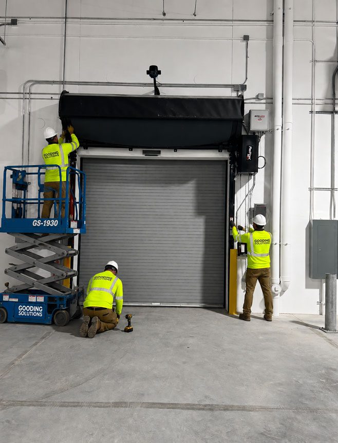 Gooding Solutions technicians installing a commercial roll-up door in industrial facility.