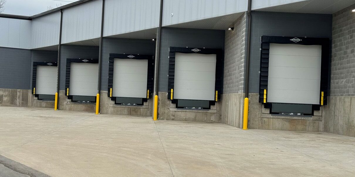 Modern warehouse loading dock doors with dock seals and safety bollards installed by Gooding Solutions.